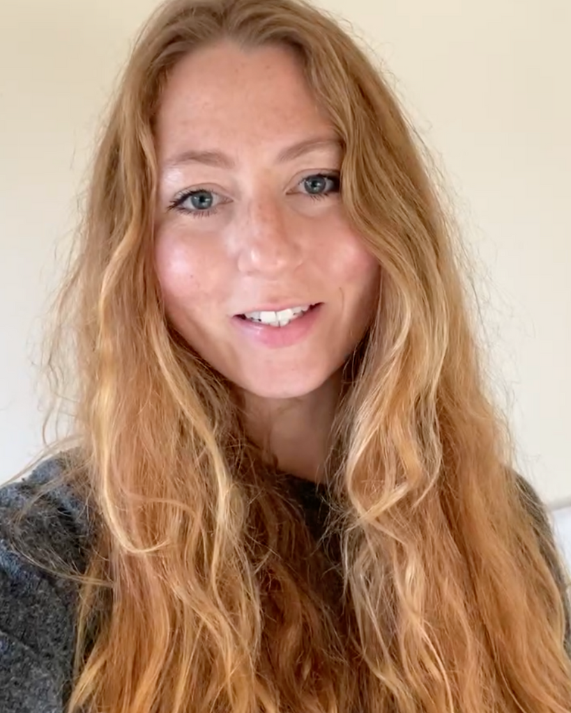 woman with long wavy ginger hair photographed smiling in front of a neutral coloured wall