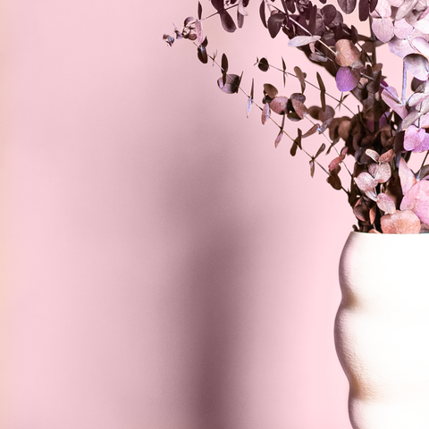 pink painted eucalyptus leaves in a white ceramic vase, photographed on the right side in front of a muted pastel pink painted wall