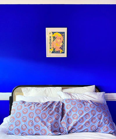 Ultramarine blue painted wall with a double bed photographed in front of it with white pillows and blue-lilac smiley face patterned bedding