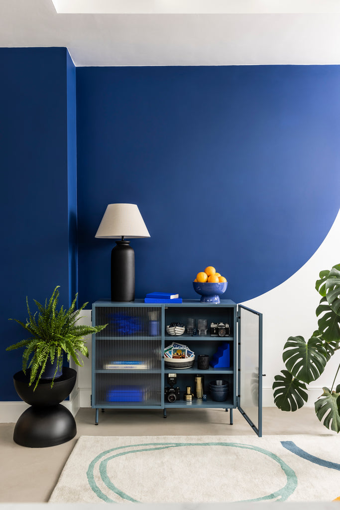 A living room wall painted in dark blue colour and white colour, with a cabinet placed in front of it