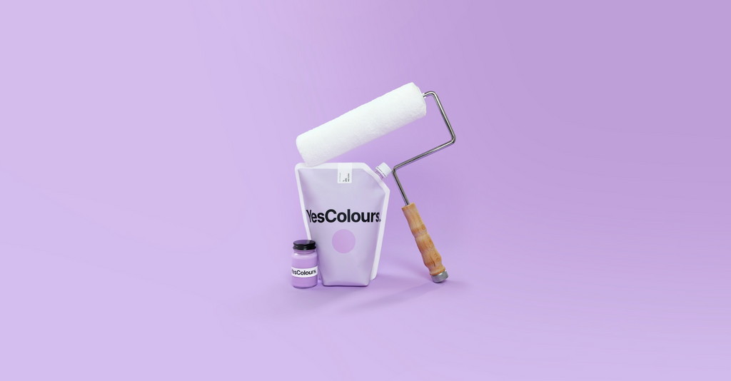 Still life product photo of YesColours paint pouch, paint sample pot in a glass jar and a paint roller, photographed in front of a pastel lilac background
