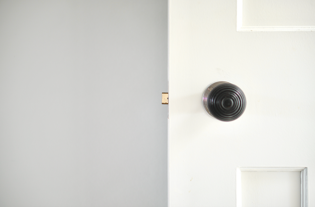 Door painted in white with a dark door handle, photographed next to a wall painted in a neutral paint colour with a hint of grey