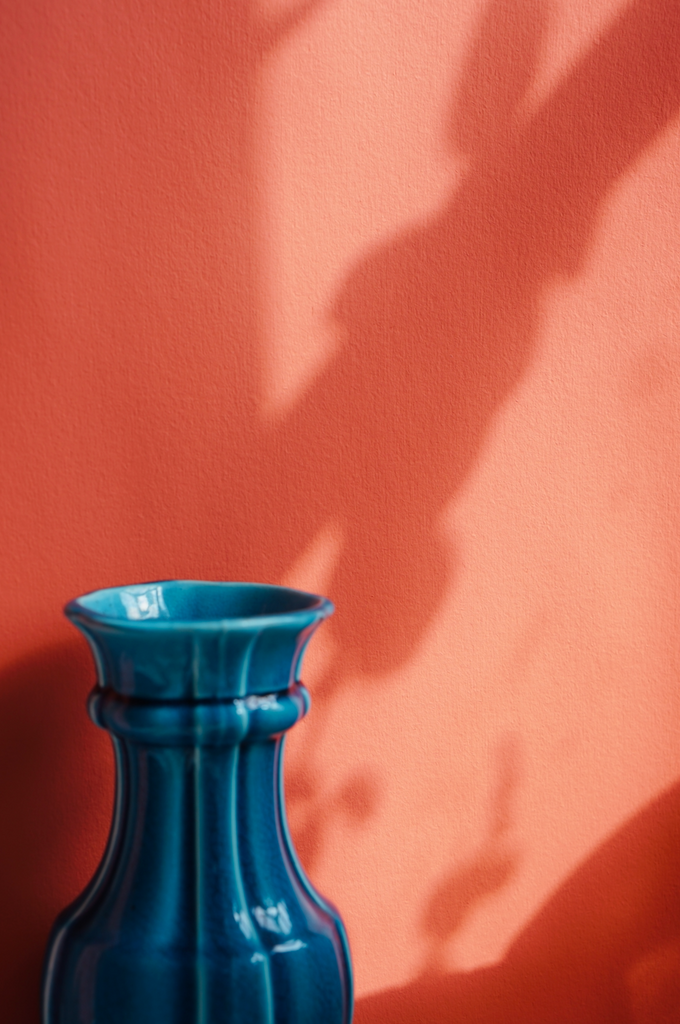 Solid ceramic vintage teal vase photographed in the bottom left corner of a coral orange painted background