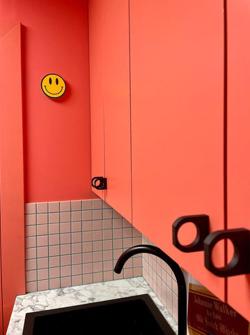 corner of s small utility room with cupboards in a coral orange colour and small square tiles as a backtop