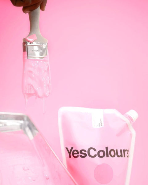 YesColours paint pouch photographed next to a metal paint tray filled with Joyful Pink pastel pink paint, with a paint brush covered in pink paint, all placed in front of a pink-coloured background