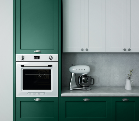a minimalist kitchen with dark green painted cupboards, integrated oven on the left side, white kitchen cupboards in the middle and a concrete blacktop and countertop with a white Smeg mixer and small vase placed on top