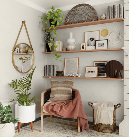 Neutral coloured boho-inspired living room corner with three wooden shelves on the wall, monochrome minimalistic prints, round hanging mirror on the wall, leafy plants and rattan chair