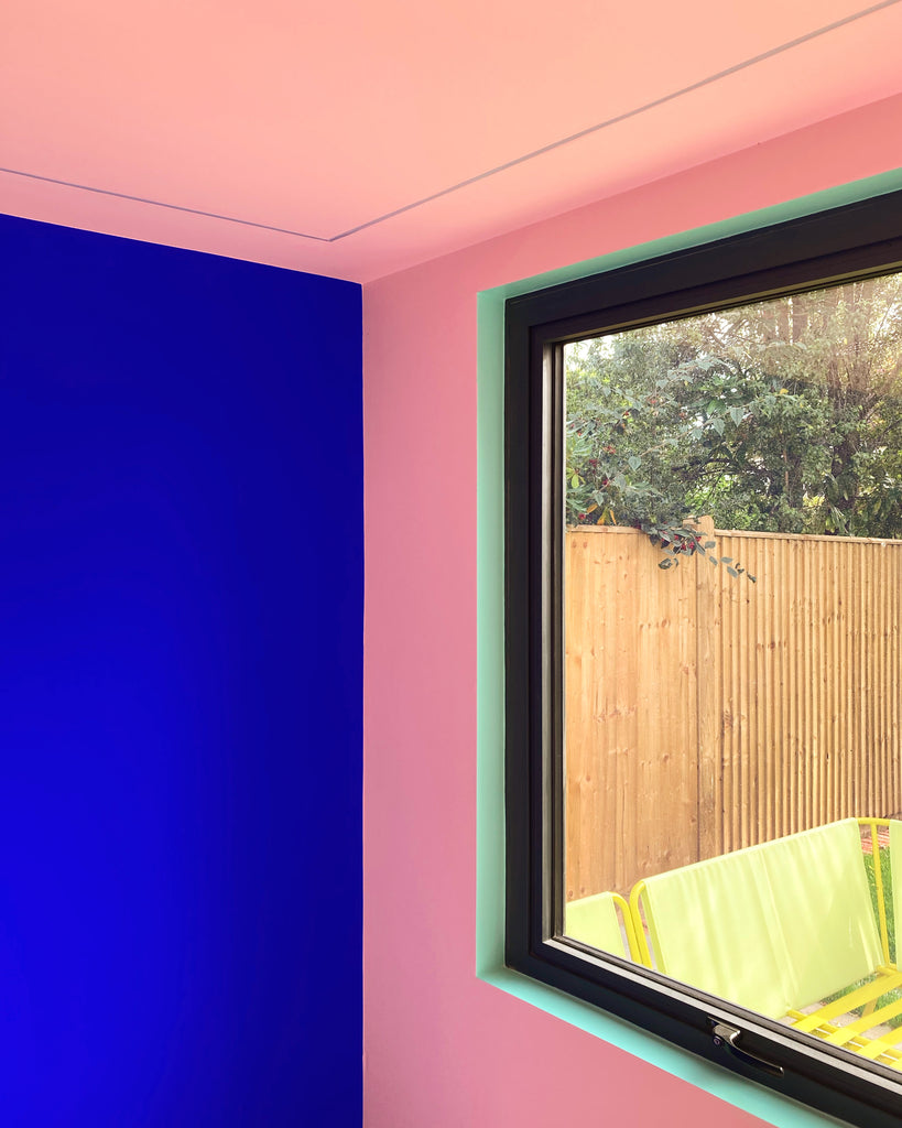 Walls painted in electric blue paint colour and peachy pink paint colour, with a window next to them, window frame painted in mint green colour