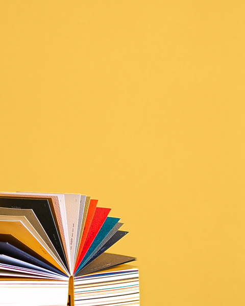 An open book with fan-spread colourful pages, photographed in front of a muted yellow wall