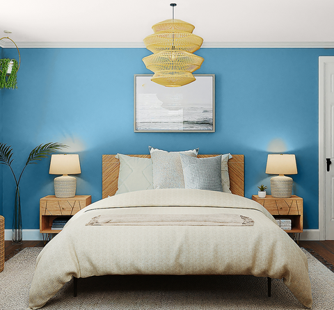 Photo of a spacious room with wooden bed placed in the middle, surrounded by low wooden bedside tables on each sides with small lamps placed on each of them, photographed in front of a muted blue wall with a white ceiling and a tiki rattan-inspired lampshade