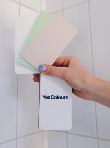 close up of a peach, green and white colour swatches held in front of a white tiled wall