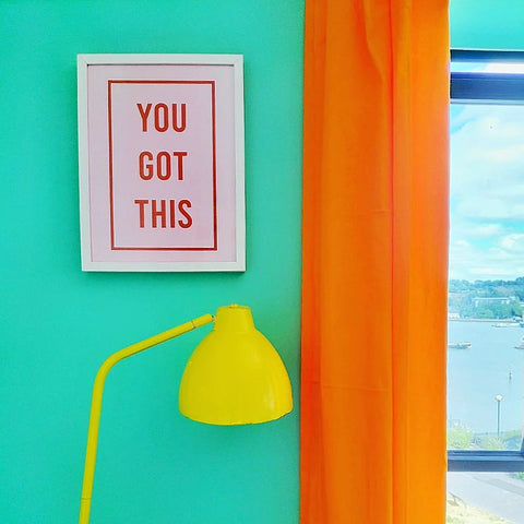 bedroom corner with walls in bright mint green colour, bright orange coloured curtains on the right and a typography art print on the left reading 'you got this'