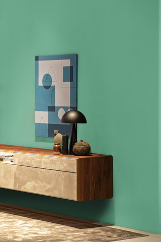 dark hallway corner with a wall painted in a teal green colour, wooden mid-century built in sideboard, vintage accessories placed on top of it and a geometric artwork in white and blue on the wall