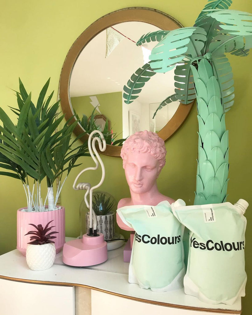 Photo of YesColours paint pouches placed on a white chest of drawers in front of an olive green wall with a mirror on it