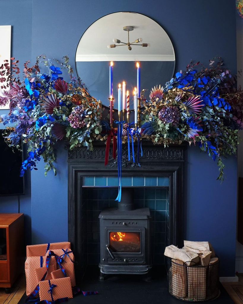 Dark blue painted wall with a black fireplace, decorated with a colourful Christmas mantel, candles and dried flowers painted with YesColours paint colours