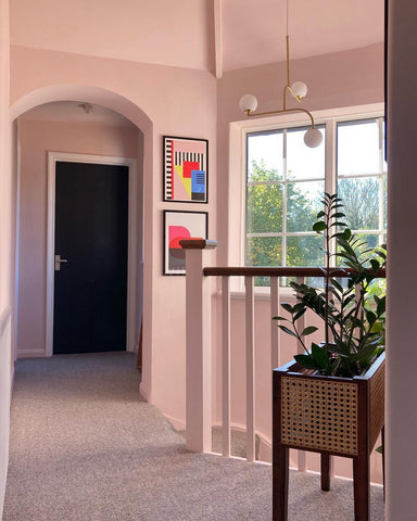 bright hallway in a house with walls painted in a warm peach paint colour, decorated with art prints and greenery