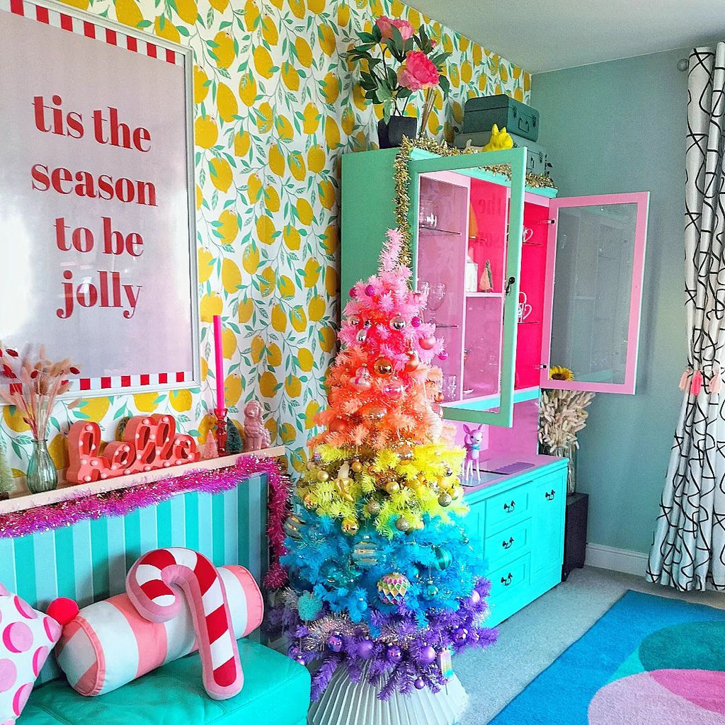 Dining room painted in bright colours - mint green, pink and lilac, with a colourful wallpaper, Christmas decoration and a rainbow-coloured Christmas tree