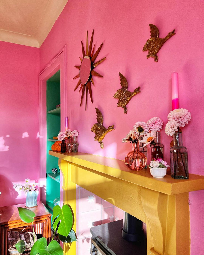 living room painted in bright pink colour with green shelves and yellow fireplace, decorated with brass stars on the wall