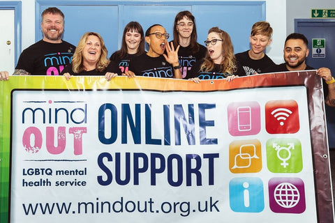 photography of eight people posing in front of a blue wall and holding a banner that says MindOut Online Support