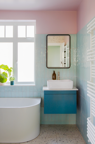 a light and airy bathroom with light pink coloured wall, mint green tiles and under sink cabinet painted in teal colour
