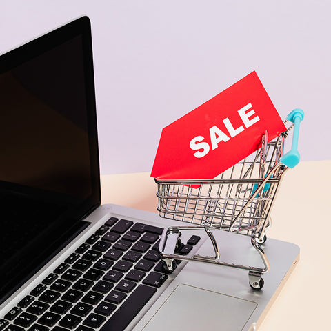 small shopping cart with sale sign sitting on a laptop