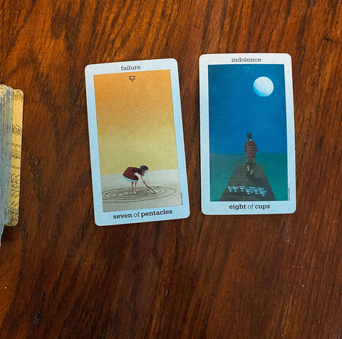 Two cards from the Sun and Moon tarot deck on a mahogany wood floor.