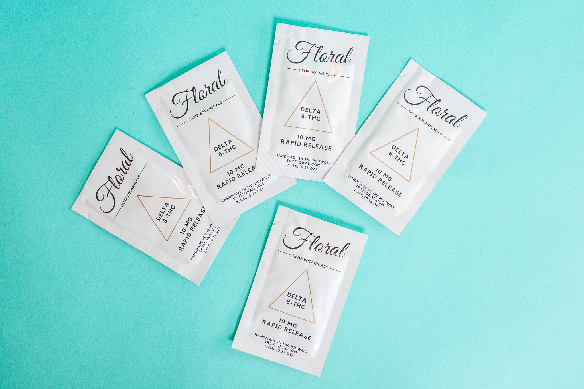 Packets of Floral Beverages' Floral Cocktail Enhancers laying against a turquoise background.