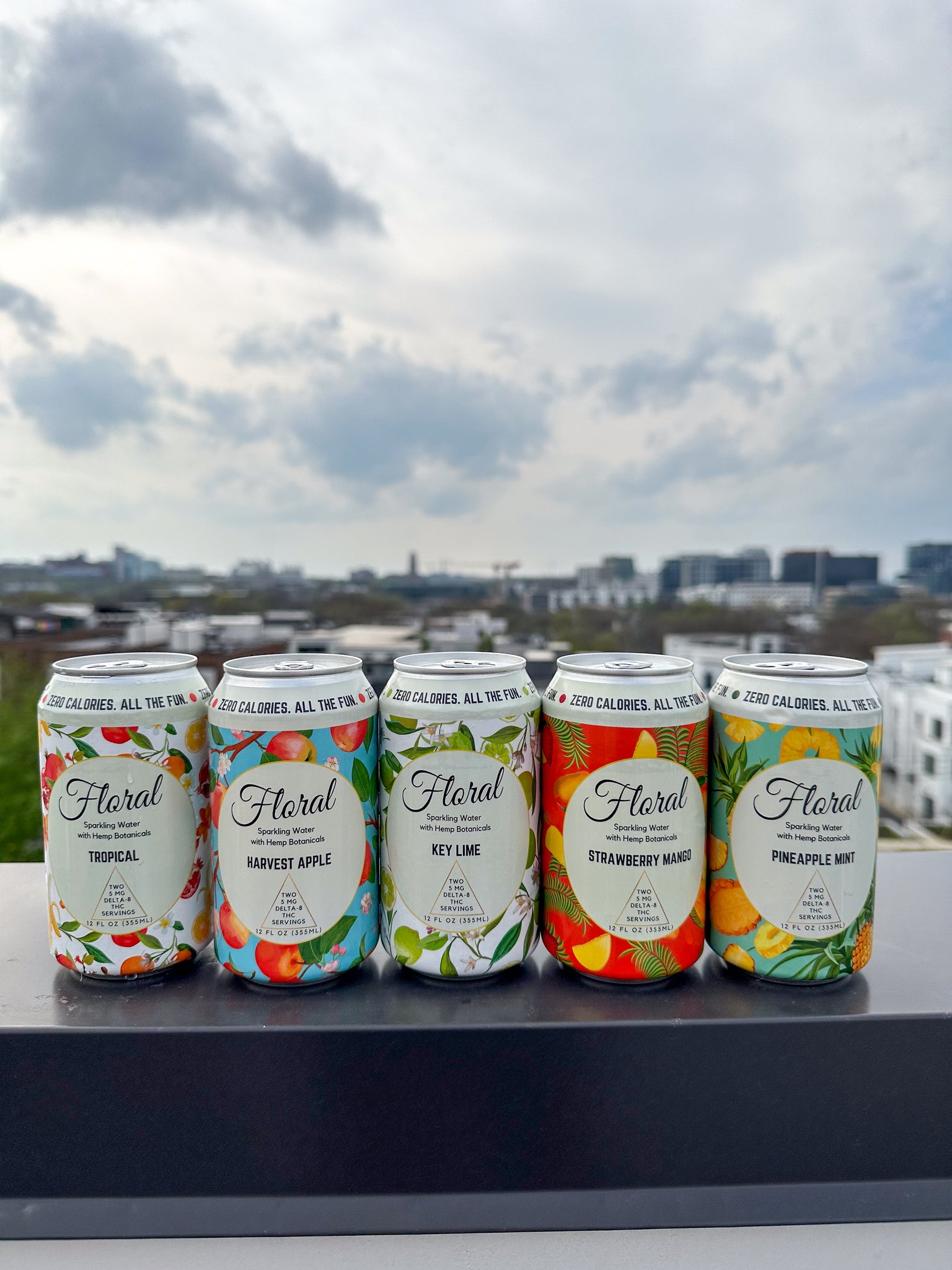 Cans of Floral Beverages THC seltzers lined up on a railing outside on a cloudy day