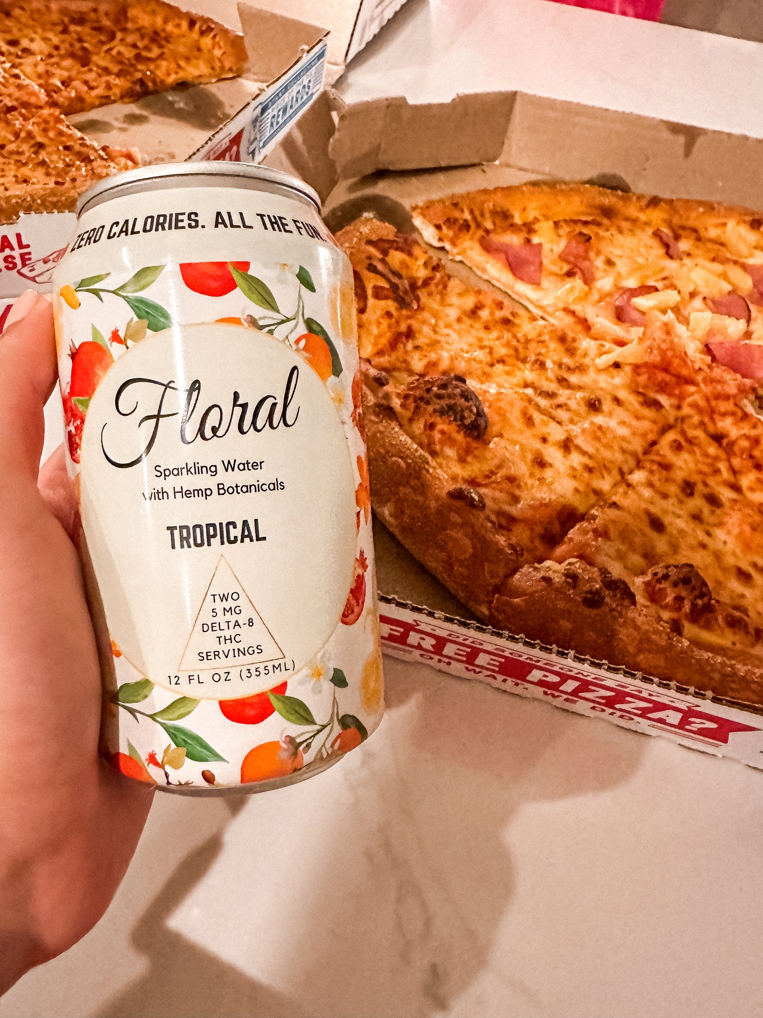 A can of Floral Beverages Tropical can beside an open box of cheese pizza.