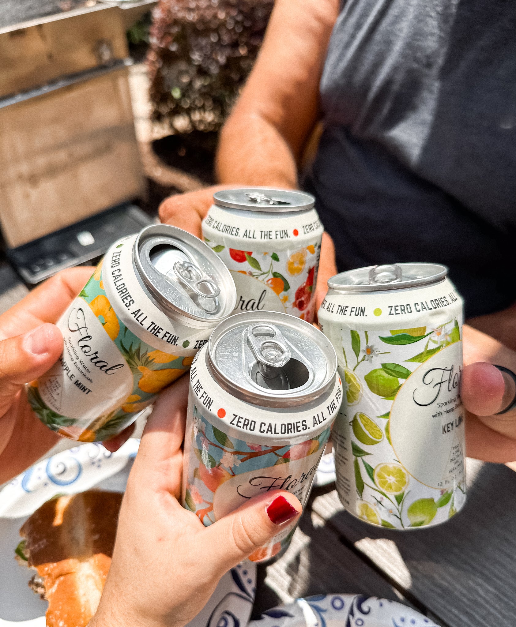 Four friends are clinking cans of Floral Beverages THC-infused seltzers together.
