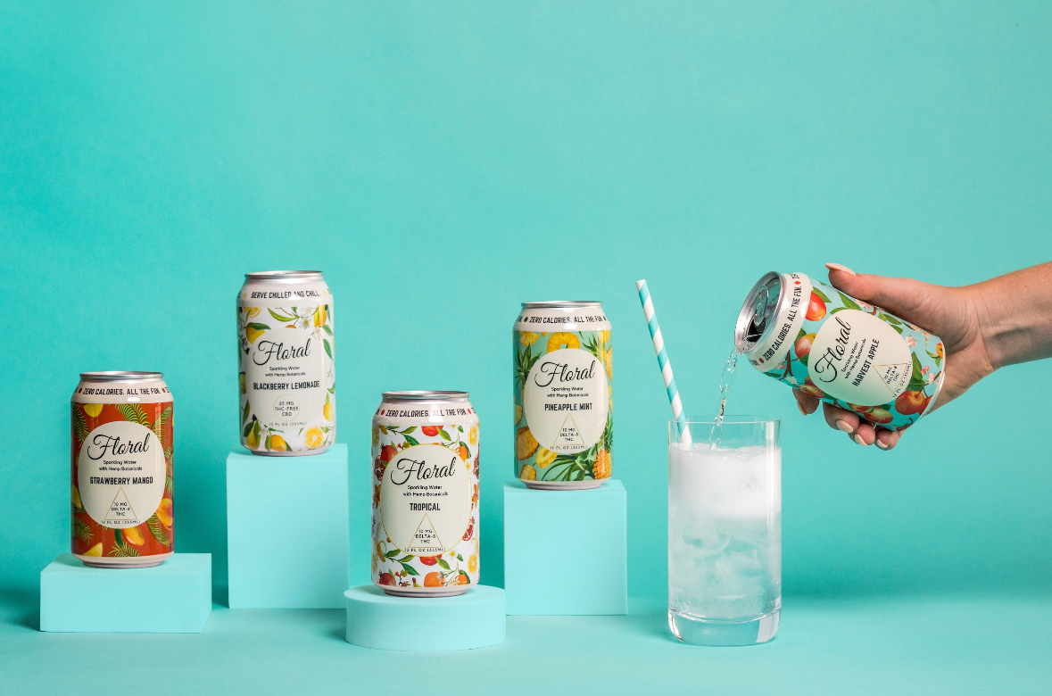 A hand pouring a can of Floral Beverage's Harvest Apple Seltzer into a glass with a straw. Several other cans of flavors are sitting beside.