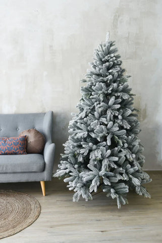 Weihnachtsbaum künstlich mit Schnee neben einer Couche auf Laminat Boden und vor Grauer Wand
