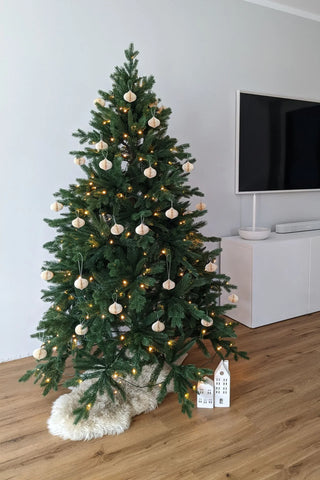 Weihnachtsbaum künstlich wie echt vor weißer Wand, auf einem Fell mit Geschenk darunter, Beleuchtet mit LEDs