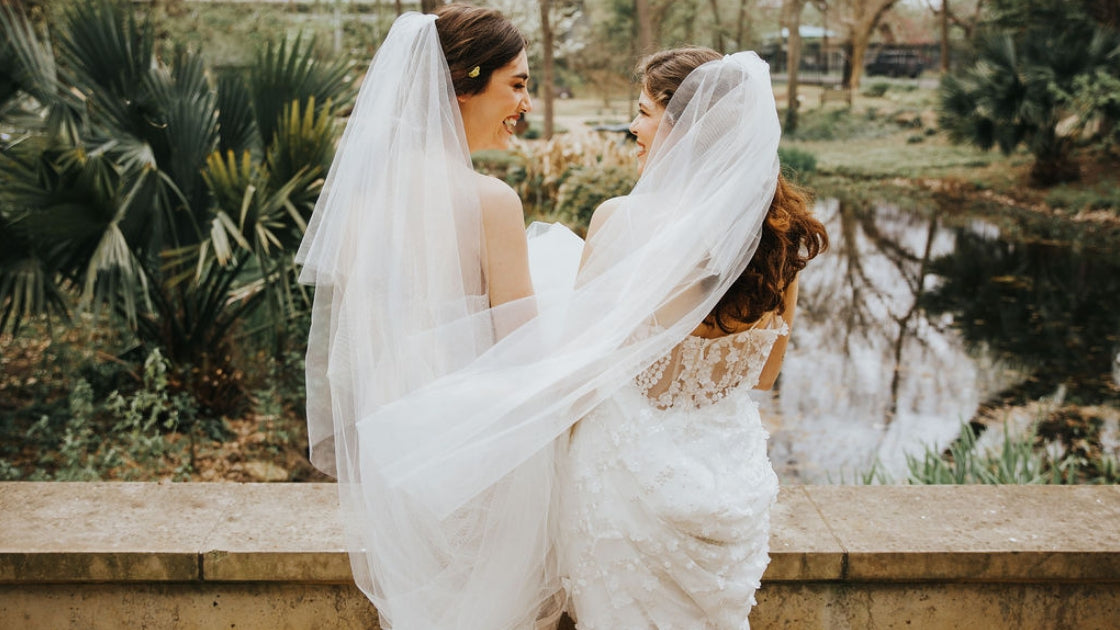 Two brides are better than 1 facing back in revelry form fitting wedding dresses laughing and posing on wedding day in veils