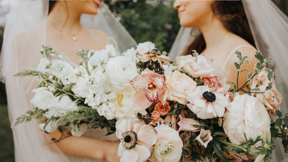 Two brides are better than 1 brides smiling looking at each other with love holding florals