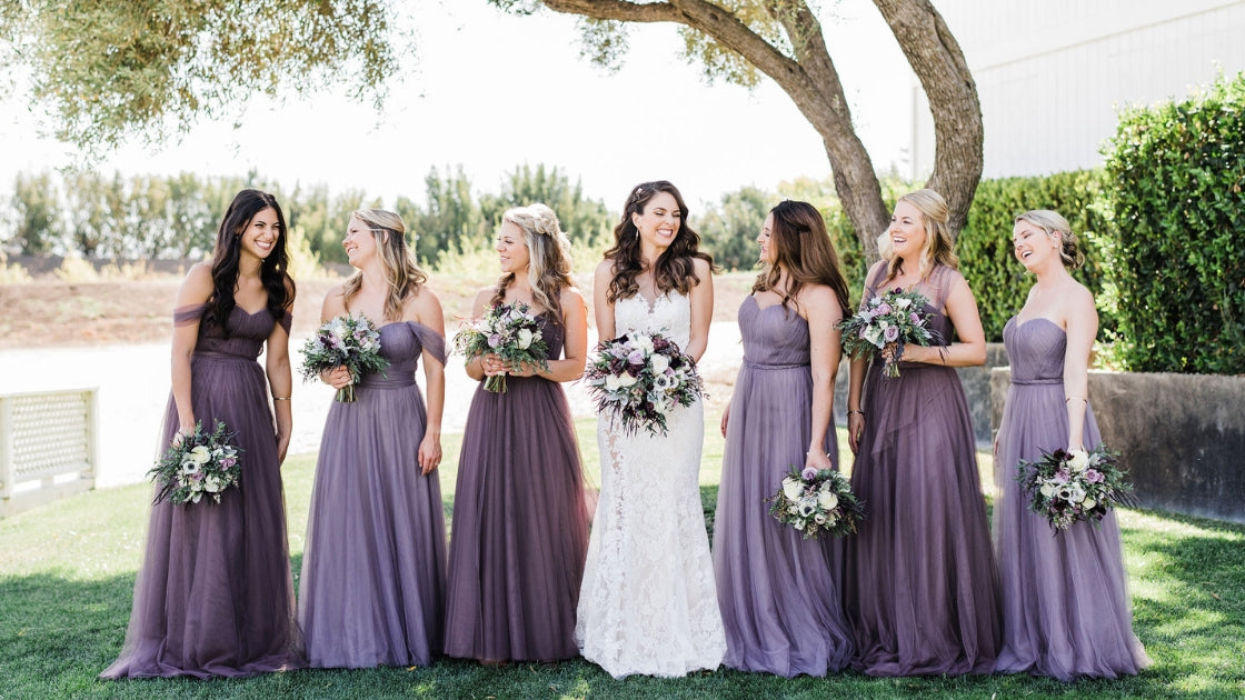 Brunette bride in lace wedding dress six bridesmaid in different purple hue tulle rosalie dresses revelry love wedding day