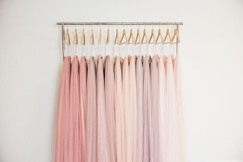 Different shades of blush and pink dresses hanging on wood hangers with white background