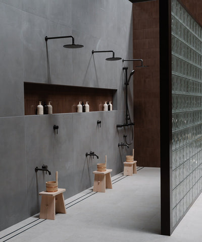 Japanese onsen-inspired showers at Ember Bathhouse, featuring wooden stools and buckets, set against serene, earth-toned tiles, emphasizing the bathhouse's blend of traditional and modern design elements.