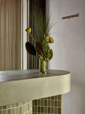 Closer view of the reception desk, showcasing its vibrant green tiles and custom concrete benchtop, elegantly decorated with native Australian flowers, adding a touch of natural beauty to the welcoming area.