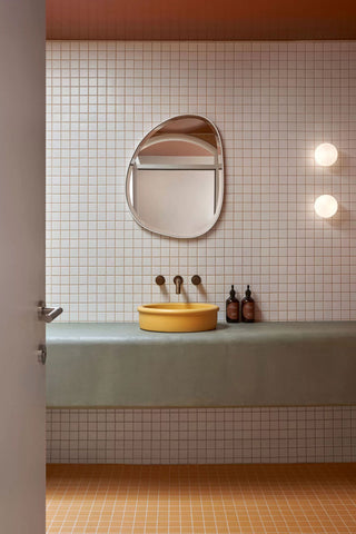 Bathroom showcasing a custom Nood Co Tubb in 'Sunny Yellow,' set against a backdrop of white square tiles with orange grout. The space is further defined by an orange ceiling, yellow floor, and a bespoke wall-to-wall concrete vanity, creating a harmoniously vibrant aesthetic.