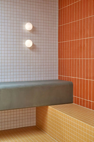 Interior design featuring two types of tiles: orange subway tiles alongside white square tiles accented with orange grout, all set above yellow polished concrete floors for a cohesive, vibrant look.