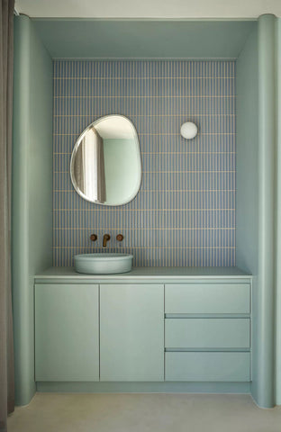 Powder blue bathroom, elegantly appointed with a Tubb in Powder Blue, complemented by curved custom cabinetry in a similar shade, an organic-shaped mirror, and sophisticated brass tapware, all harmonizing to create a serene and stylish space.