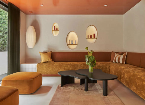 Reception area at Indie Spa showcasing a warm palette of burnt orange and mustard hues, complemented by a plush, curved couch, a vibrantly colored ceiling, and unique, imperfectly rounded wall niches.