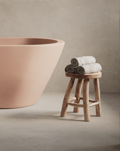 Juno Concrete Bathtub in Blush Pink finish in a moody setting with rendered walls and archway.