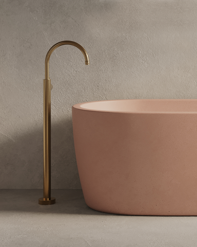 Juno Concrete Bathtub in Blush Pink finish in a moody setting with rendered walls and archway.