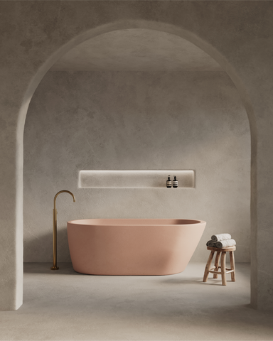 Juno Concrete Bathtub in Blush Pink finish in a moody setting with rendered walls and archway.