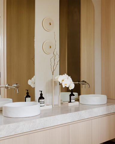 A close-up of the ensuite bathroom vanity area, showcasing the beautiful Slip basins by Nood Co in Ivory, fluted glass, and steel doors. The Soktas hand-blown lighting adds a touch of sophistication and warmth to the space.