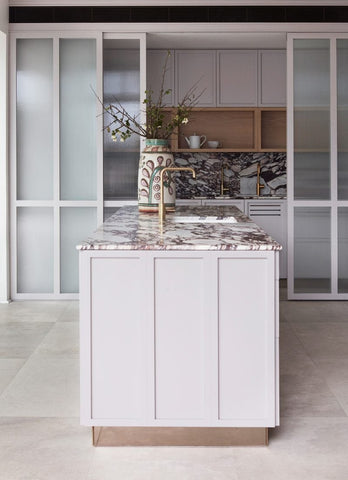 From another angle, the kitchen reveals fluted glass doors that conceal a hidden pantry. These elegant doors add a touch of privacy and sophistication to the space while providing easy access to a well-organized pantry behind them.