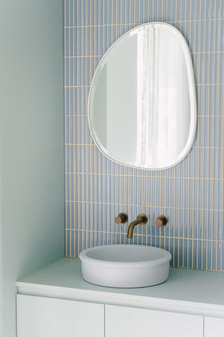 Alternate angle of the powder blue bathroom, showcasing the Tubb in Powder Blue as a focal point, with its surrounding elements of curved blue cabinetry, the organic mirror, and brass tapware, all contributing to the room's tranquil and cohesive aesthetic.