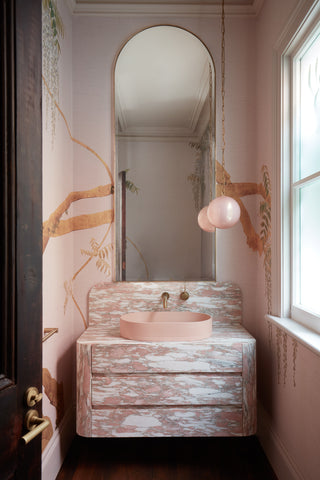 In the pink bathroom, a sense of timeless elegance prevails. A Norwegian Rose Marble vanity takes center stage, its intricate patterns and soft pink hues exuding sophistication. Above the vanity, an arch mirror reflects the room's classic charm. Brass tapware adds a warm metallic accent, while blush pink wallpaper enhances the overall aesthetic. The focal point is the Nood Co basin in Blush Pink, a modern masterpiece that harmonises with the room's vintage-inspired decor.